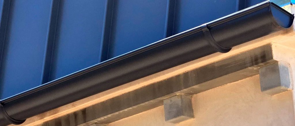 Black half-round gutter system installed on a contemporary home with a blue standing seam metal roof.