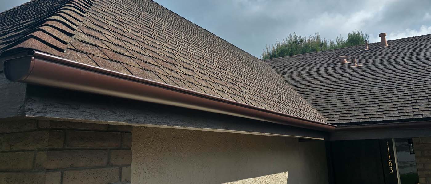 Brown half-round gutter installed on a shingle roof of a residential home.