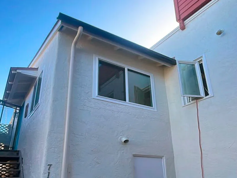 Half-round gutter along the roof edge with a champagne round downspout running down the light stucco wall.